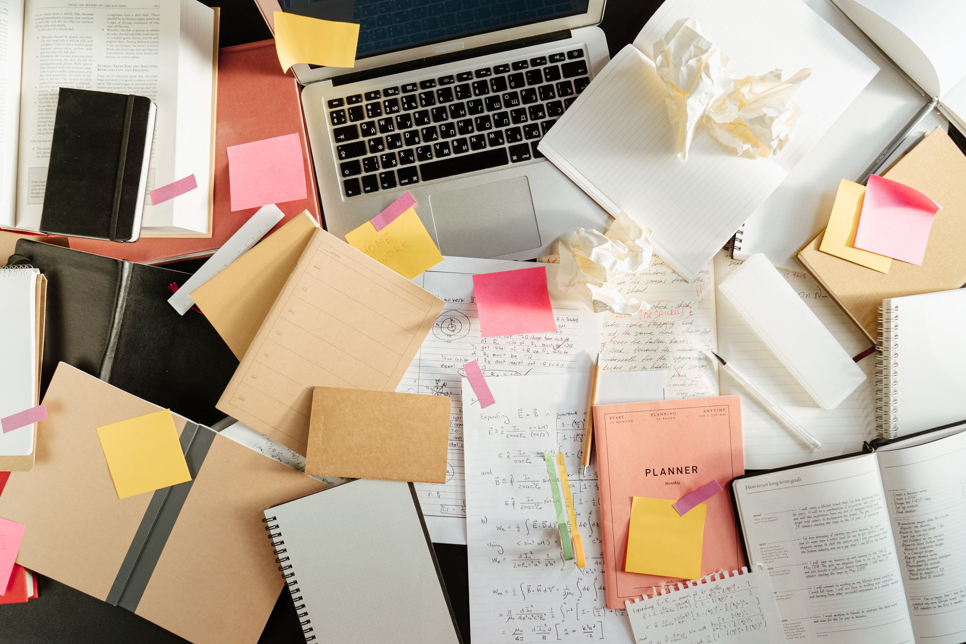 A desk cluttered with a laptop, sticky notes and loose paperwork